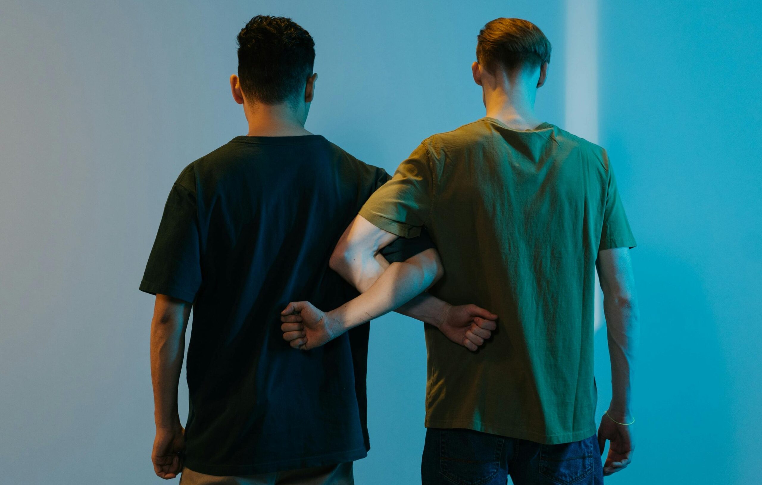 Men Standing Beside a Blue Concrete Wall linking arms considering having a bi-curious gay straight bareback bang photo by Pexel via Ron Latch