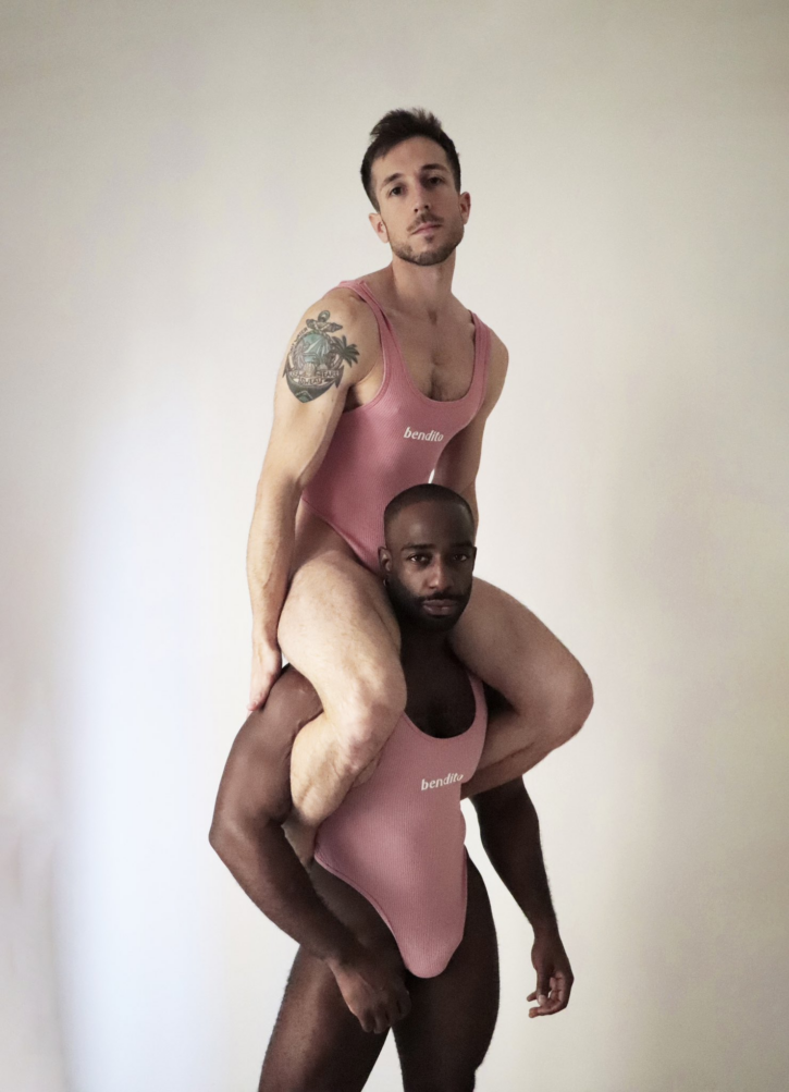 two gay male models wearing light pink barbie inspired gay body suits with the logo bendito on the front