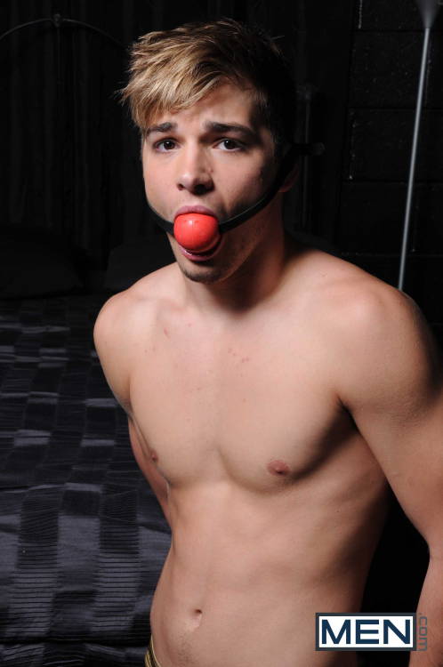 gay male blonde twink with a red ballgag in his mouth looking to the camera for men.com