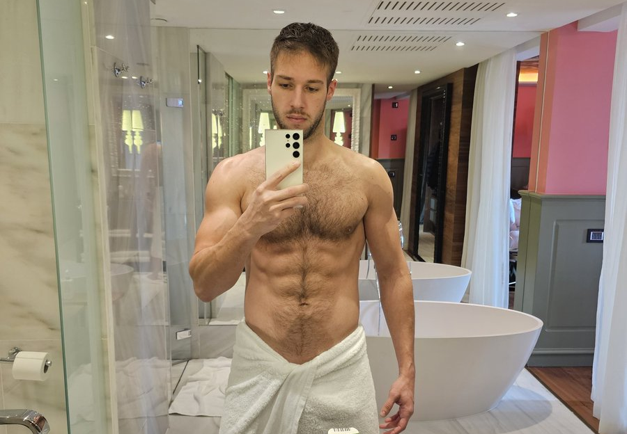 Arno Antino posing in a white towel showing off his erect cock through the fabric while taking an iphone mirror selfie in the bathroom for gay xxx onlyfans follower content