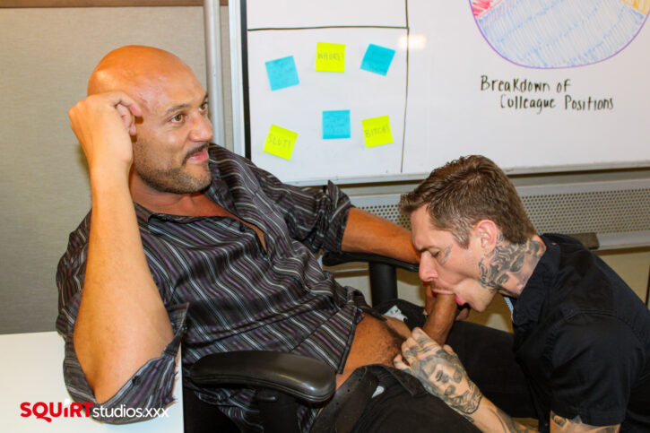 Rocky Unleashed smirking as Zak Bishop chokes on his massive dick looking over at voyeur Dallas Knoxxx watching the two fucking in the office for Squirt Studios