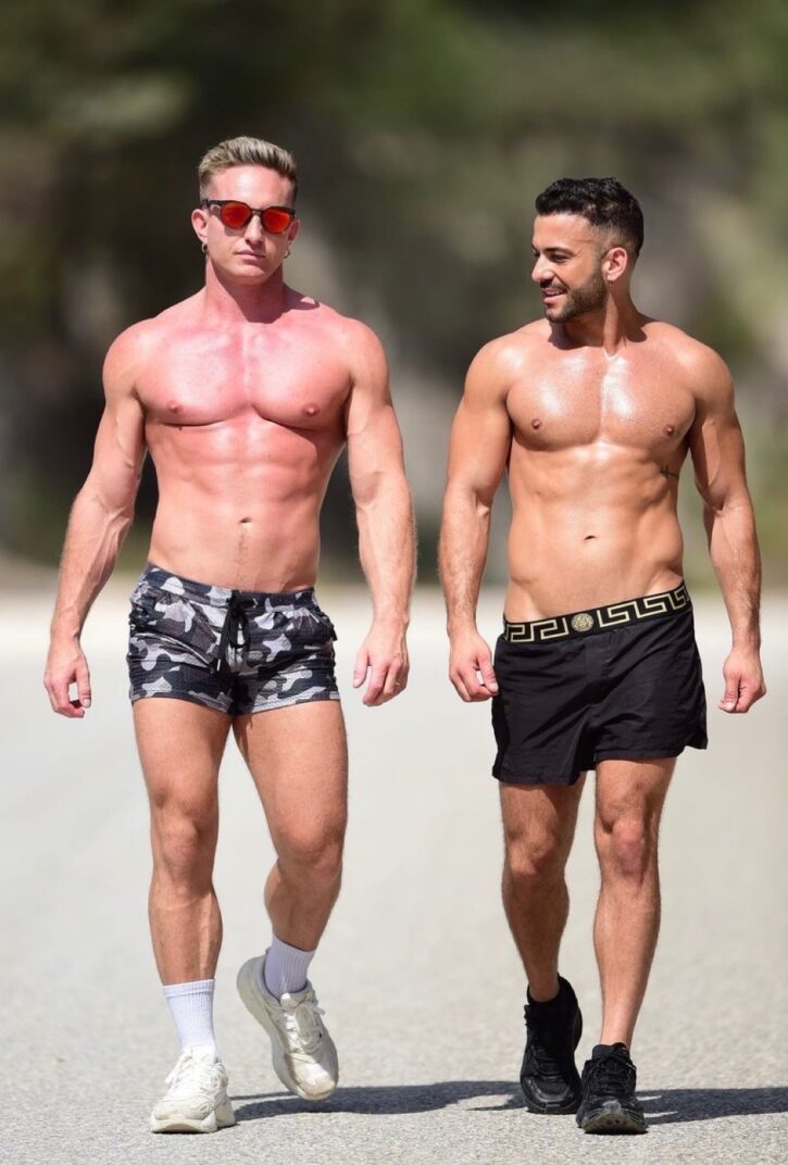 gay xxx porn and onlyfans creator Magnus Loki walking shirtless in tight camo shorts with ripped abs next to hot gay stud outdoors
