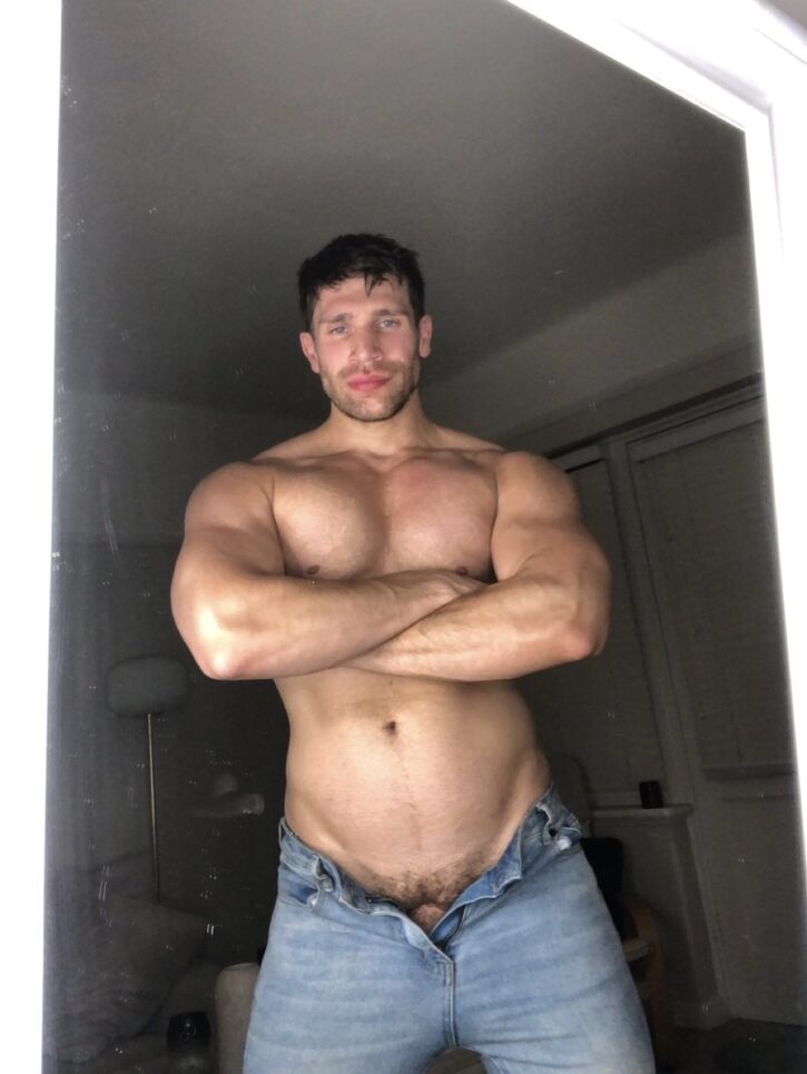 bastian kouros male OnlyFans gay porn creator shirtless in unbuttoned jeans posing with arms crossed