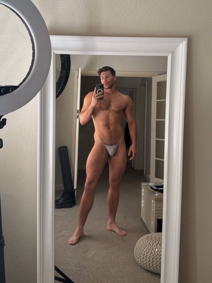 bastian kouros shirtless male OnlyFans gay porn creator posing in front of a full length mirror wearing a small grey thong