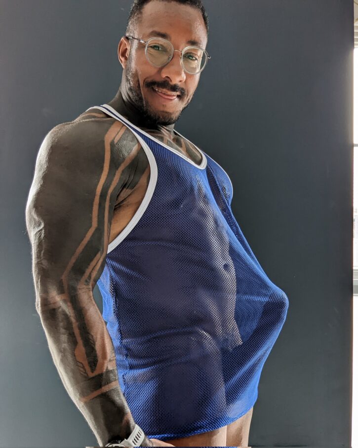 Gay porn star Amadeus in a sheer blue tank top, showing off tattoos and muscles and hard cock. OnlyFans & JustForFans content creator